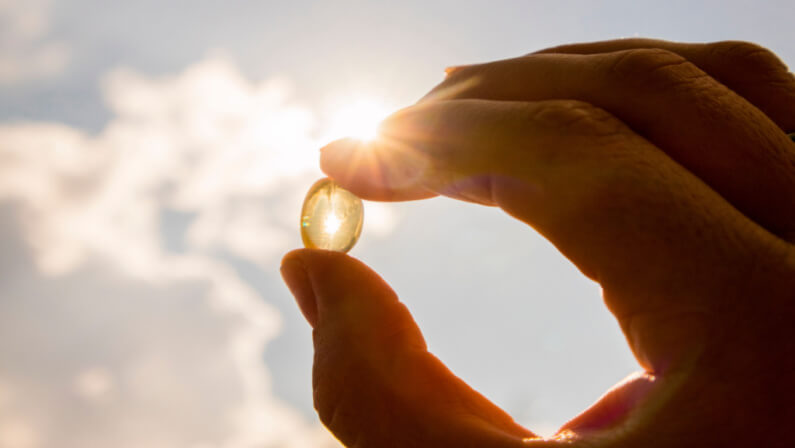 Vitamin D capsule lifted against the sunlight